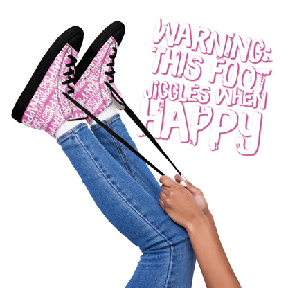 Womens feet in the air holding laces of HappyStuff pink and white high tops fun print Warning This Foot Jiggles When Happy black sole